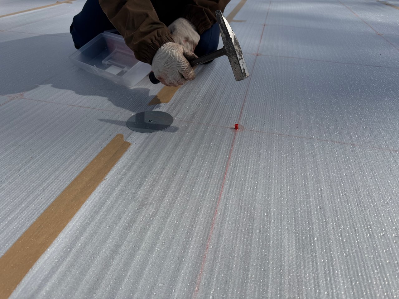 防水シートの固定部にアンカープラグを打ち込む作業。